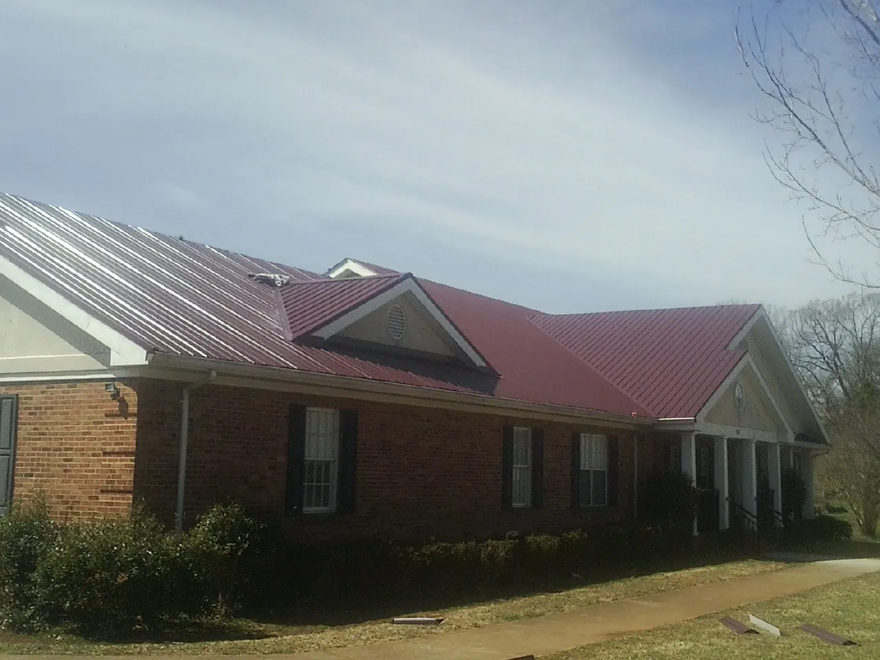 Red metal roof with gabled entries on a long brick building, from a Hail Damage Roof Repair job in Harrodsburg
