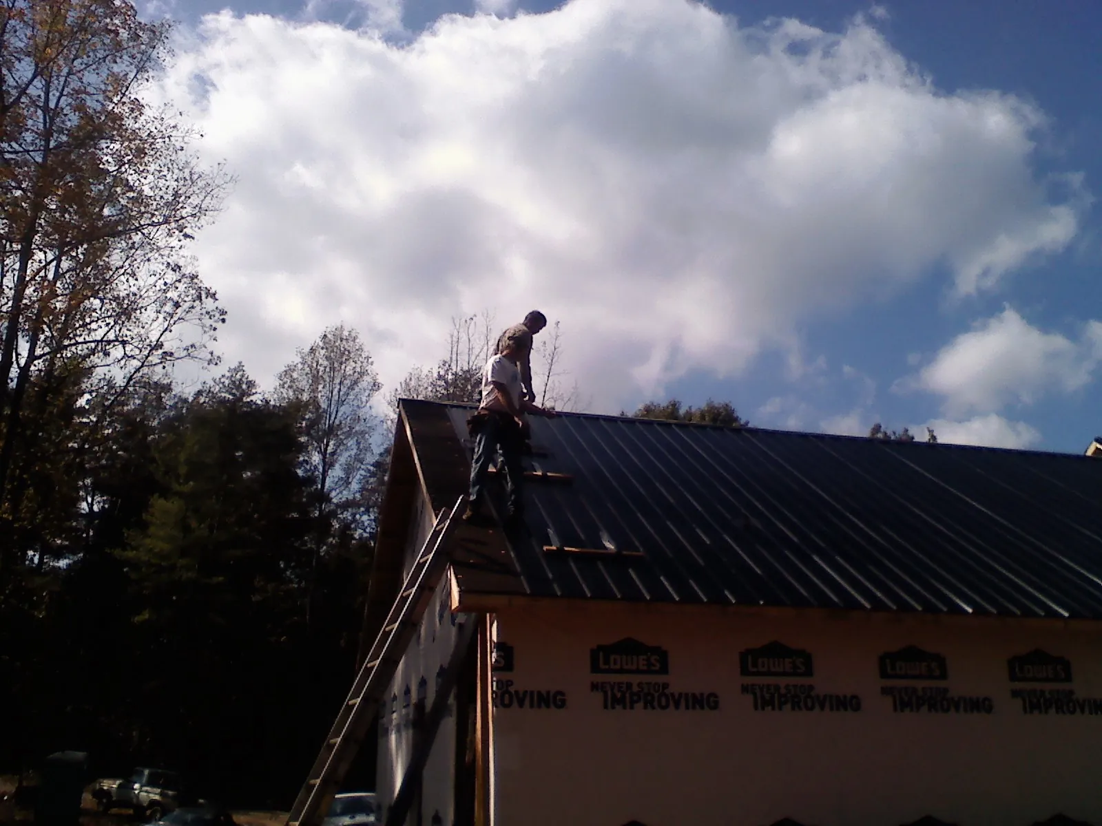Roofer fastening dark metal panels high against a cloudy sky, from a Roof Inspection job in Harrodsburg