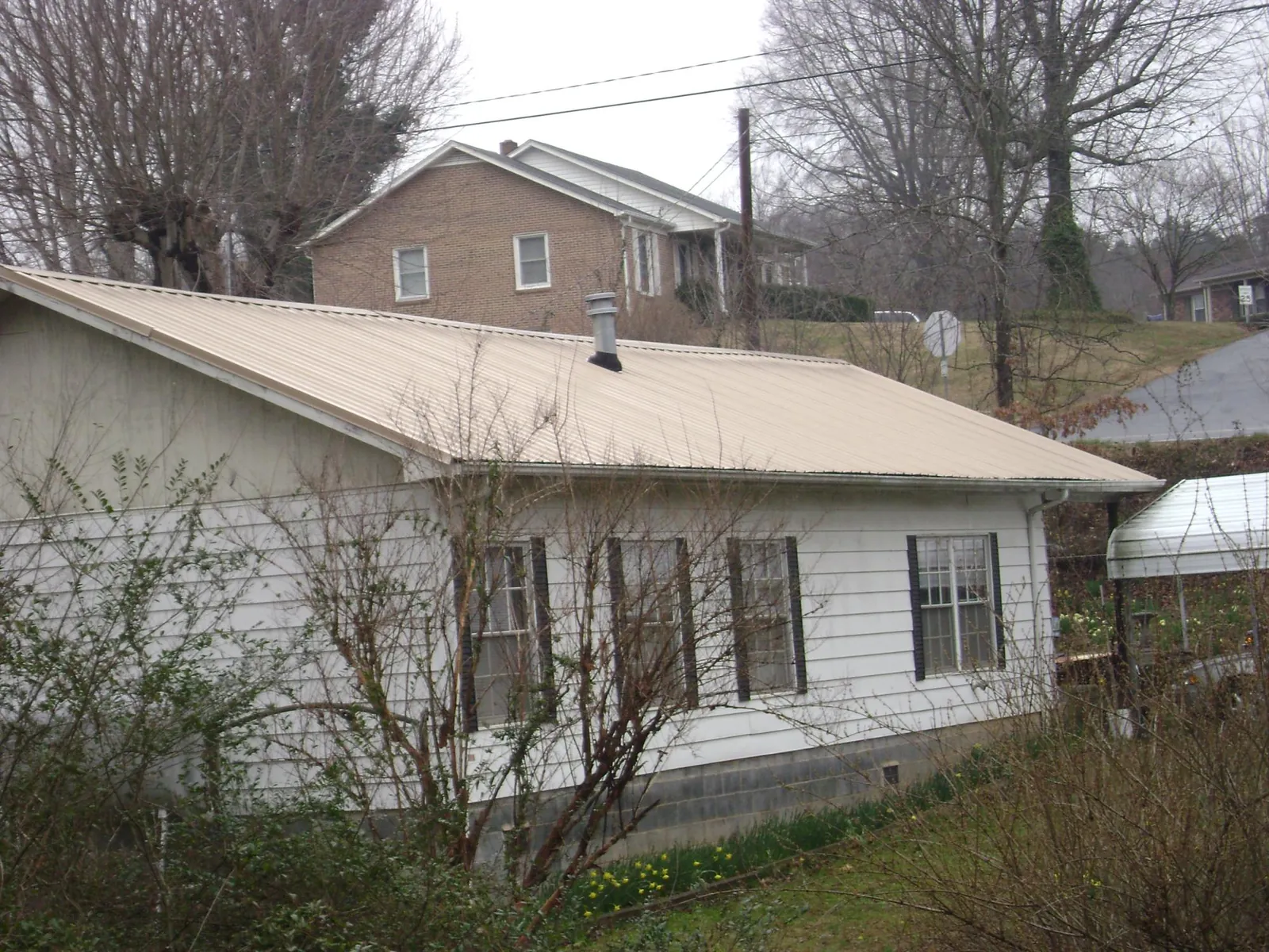 Tan metal roof on a white sided house set into a hillside — Commercial Roofing by Roofing Brothers in Harrodsburg